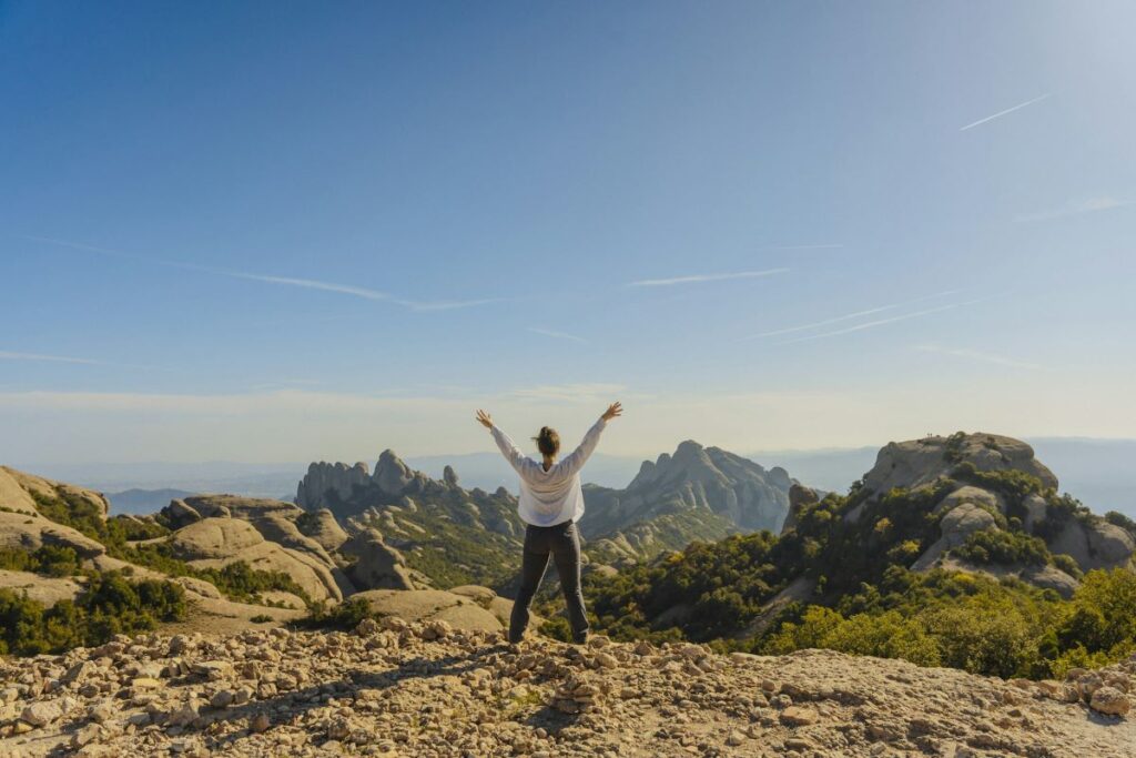 a woman on a mountain raising her arms up, depicting her resilience amidst the trials